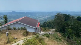 Bangunan Koperasi Desa Merah Putih (KDMP) Dusun Bukitsari, Desa Kediten, Kecamatan Plantungan, Kabupaten Kendal, terlihat dari sisi lain dengan pemandangan perbukitan dan permukiman di kejauhan, Minggu (6/9/2026). Posisi bangunan berada di kawasan berkontur miring, sementara jalan beton menghubungkan lokasi gedung dengan kawasan permukiman warga. (TribunJateng)

