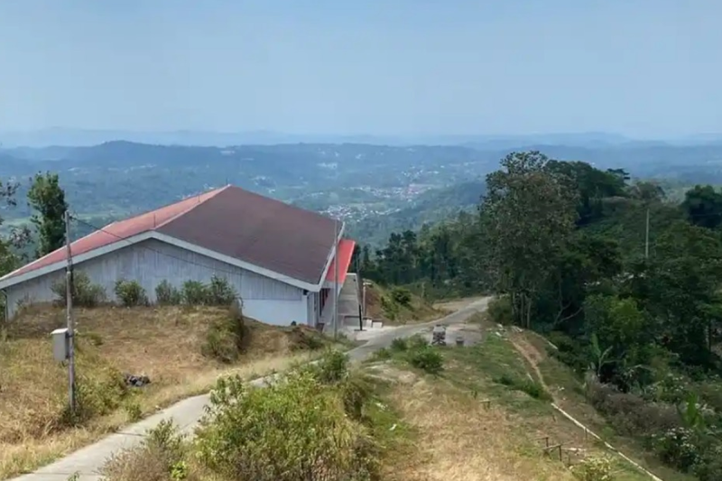 Bangunan Koperasi Desa Merah Putih (KDMP) Dusun Bukitsari, Desa Kediten, Kecamatan Plantungan, Kabupaten Kendal, terlihat dari sisi lain dengan pemandangan perbukitan dan permukiman di kejauhan, Minggu (6/9/2026). Posisi bangunan berada di kawasan berkontur miring, sementara jalan beton menghubungkan lokasi gedung dengan kawasan permukiman warga. (TribunJateng)

